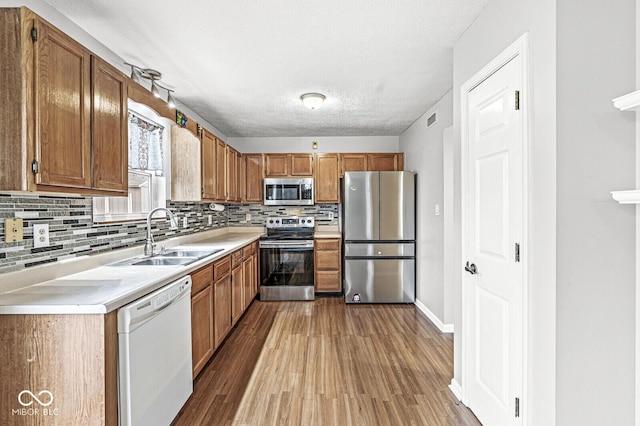 kitchen featuring sink, hardwood / wood-style flooring, a textured ceiling, appliances with stainless steel finishes, and tasteful backsplash