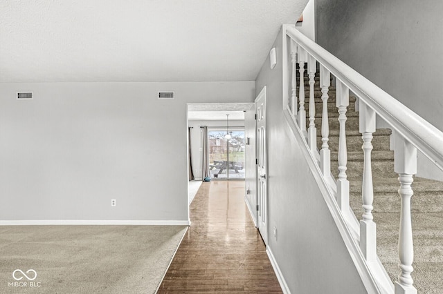 stairway featuring hardwood / wood-style floors, a textured ceiling, and an inviting chandelier