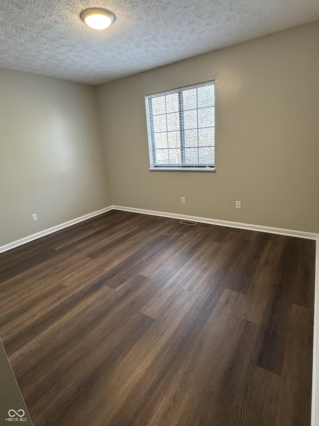 spare room featuring dark hardwood / wood-style flooring and a textured ceiling