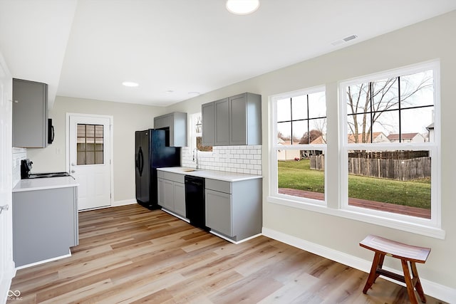 kitchen featuring decorative backsplash, light wood-type flooring, gray cabinetry, and black appliances