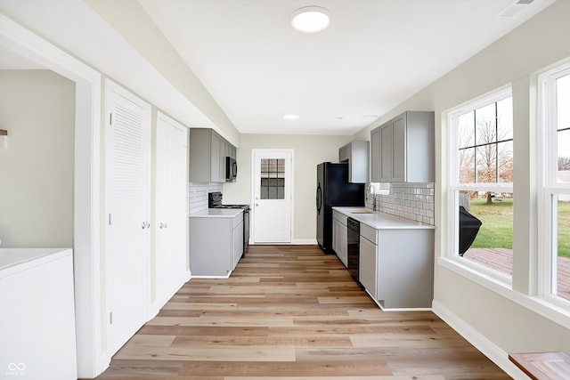 kitchen featuring gray cabinetry, light hardwood / wood-style flooring, washer / dryer, decorative backsplash, and black appliances