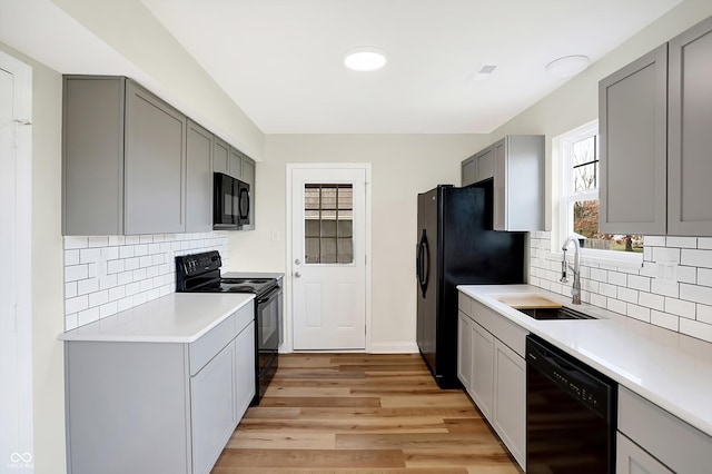 kitchen with light wood-type flooring, sink, backsplash, and black appliances