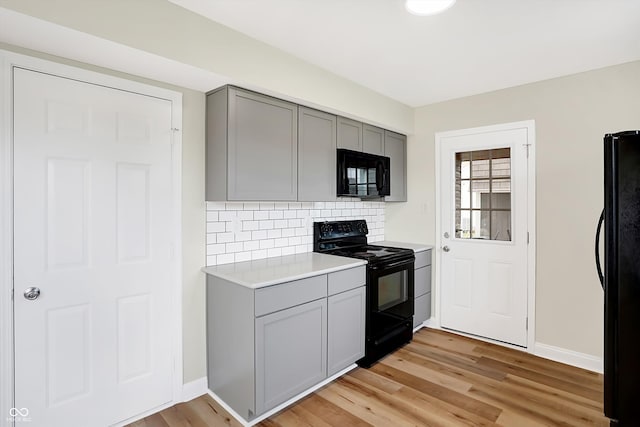 kitchen with tasteful backsplash, gray cabinets, light hardwood / wood-style flooring, and black appliances