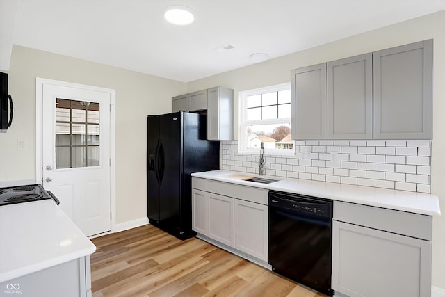 kitchen with gray cabinetry, sink, tasteful backsplash, light hardwood / wood-style floors, and black appliances