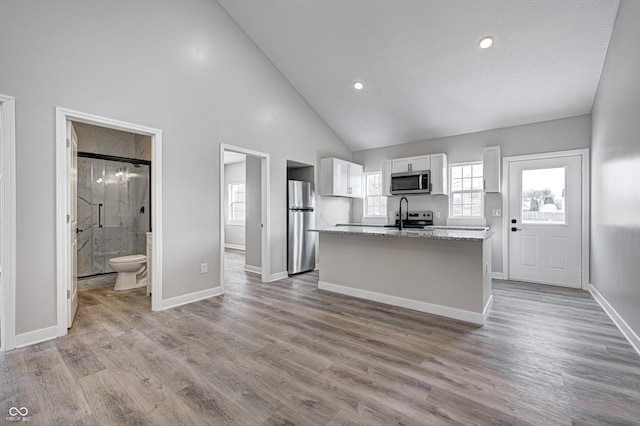 kitchen featuring high vaulted ceiling, light stone countertops, an island with sink, white cabinetry, and stainless steel appliances