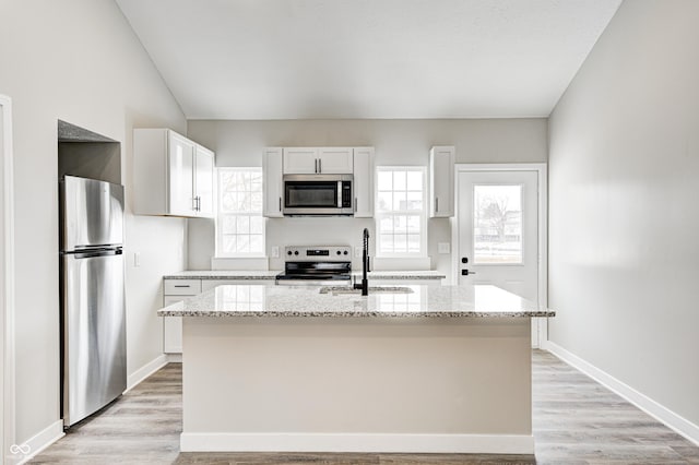 kitchen with light stone counters, white cabinetry, a kitchen island with sink, and appliances with stainless steel finishes