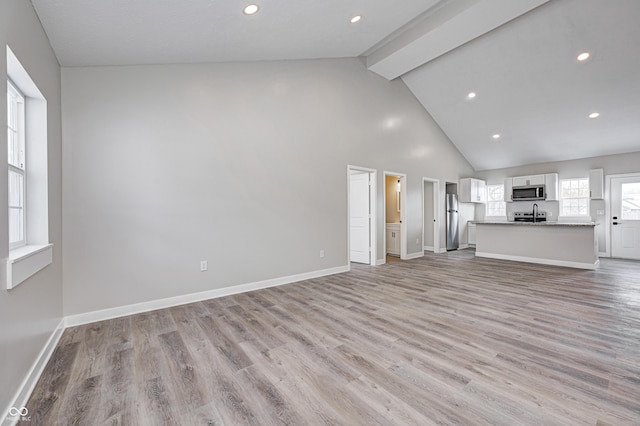 unfurnished living room featuring beam ceiling, light wood-type flooring, and high vaulted ceiling