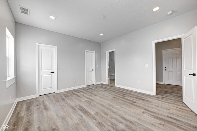 unfurnished bedroom featuring light hardwood / wood-style floors, a textured ceiling, and connected bathroom