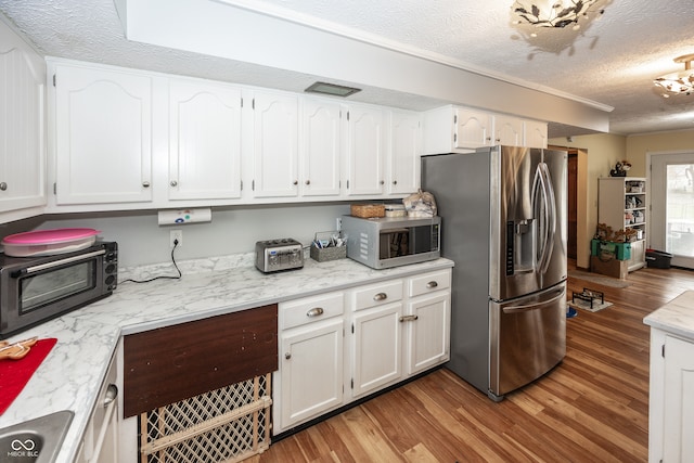 kitchen featuring light stone countertops, a textured ceiling, stainless steel appliances, hardwood / wood-style flooring, and white cabinets