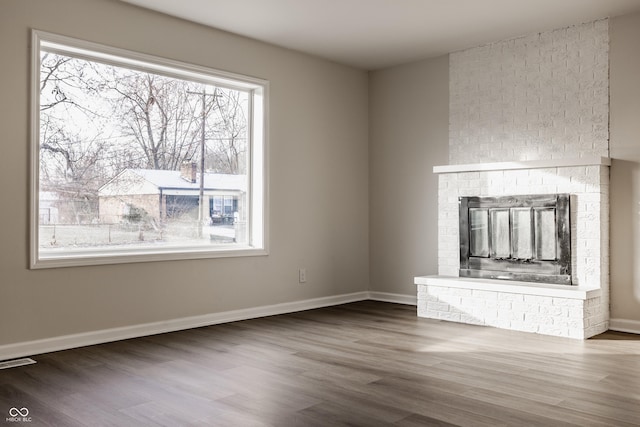 unfurnished living room with dark hardwood / wood-style flooring, a wealth of natural light, and a brick fireplace