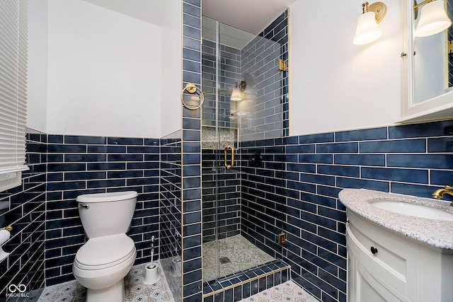 bathroom with vanity, tile patterned floors, toilet, tile walls, and a shower with shower door