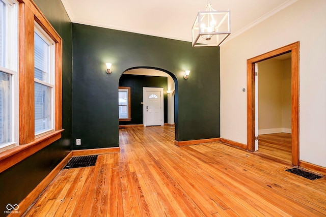 spare room featuring a chandelier, a wealth of natural light, crown molding, and light hardwood / wood-style floors