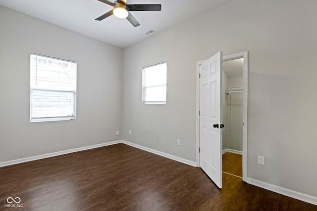 unfurnished bedroom with ceiling fan, a spacious closet, and dark wood-type flooring