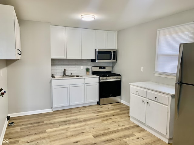 kitchen with stainless steel appliances, white cabinetry, light hardwood / wood-style floors, and sink