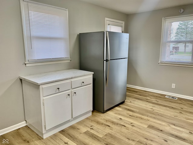 kitchen with white cabinetry, stainless steel fridge, light hardwood / wood-style floors, and light stone counters