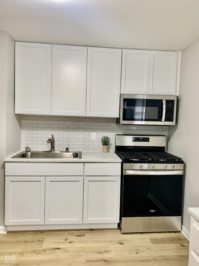 kitchen with sink, light wood-type flooring, tasteful backsplash, white cabinetry, and stainless steel appliances