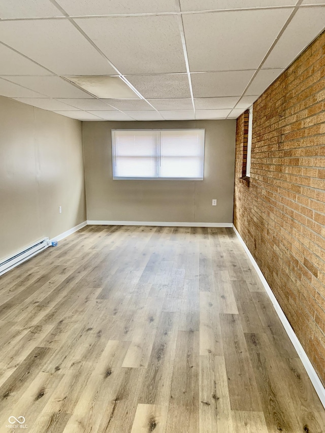 spare room with a paneled ceiling, wood-type flooring, brick wall, and a baseboard heating unit