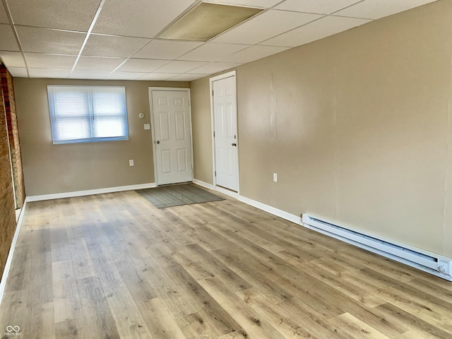 spare room featuring light wood-type flooring, a baseboard radiator, and a paneled ceiling