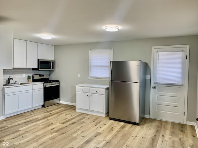 kitchen with white cabinets, sink, appliances with stainless steel finishes, tasteful backsplash, and light hardwood / wood-style floors