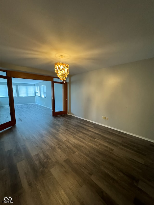 spare room with a notable chandelier and dark hardwood / wood-style flooring