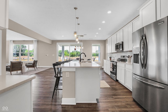 kitchen with hanging light fixtures, a healthy amount of sunlight, stainless steel appliances, and a kitchen island with sink