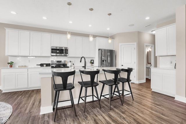 kitchen featuring white cabinetry, dark wood-type flooring, hanging light fixtures, a center island with sink, and appliances with stainless steel finishes