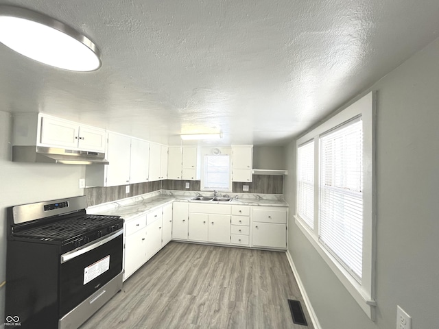 kitchen featuring white cabinets, sink, stainless steel gas stove, light wood-type flooring, and a textured ceiling