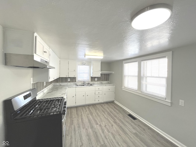 kitchen featuring light wood-type flooring, gas stove, a textured ceiling, sink, and white cabinets