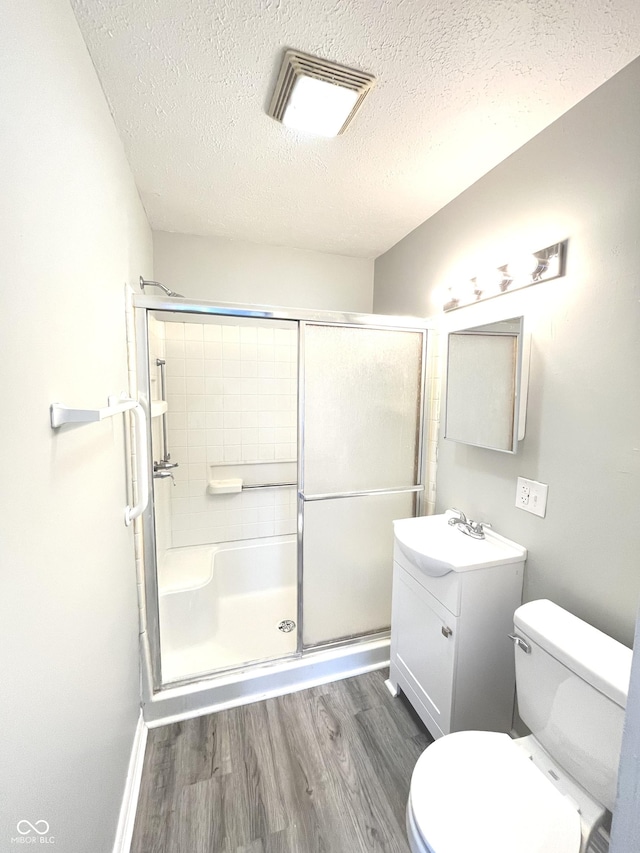 bathroom featuring hardwood / wood-style floors, a textured ceiling, toilet, vanity, and a shower with shower door