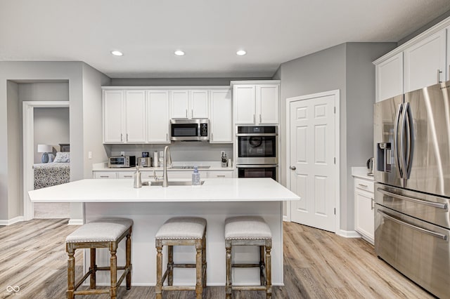 kitchen featuring light wood-type flooring, stainless steel appliances, white cabinetry, and a center island with sink