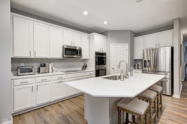 kitchen with sink, a kitchen breakfast bar, light hardwood / wood-style floors, a center island with sink, and appliances with stainless steel finishes