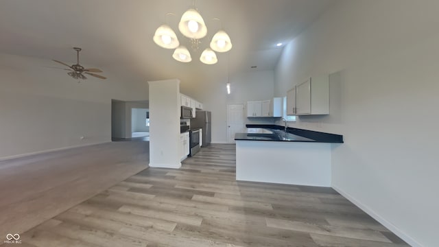 kitchen featuring a high ceiling, a sink, stainless steel appliances, white cabinetry, and open floor plan