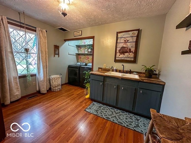 bar with washing machine and clothes dryer, sink, wood-type flooring, and a textured ceiling