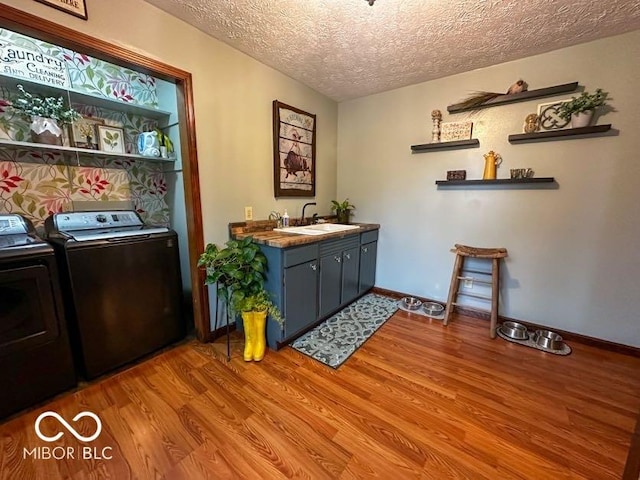 washroom with cabinets, sink, light hardwood / wood-style flooring, a textured ceiling, and washing machine and clothes dryer