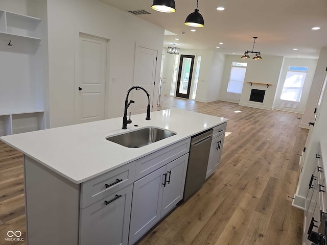 kitchen featuring sink, stainless steel dishwasher, hanging light fixtures, and an island with sink