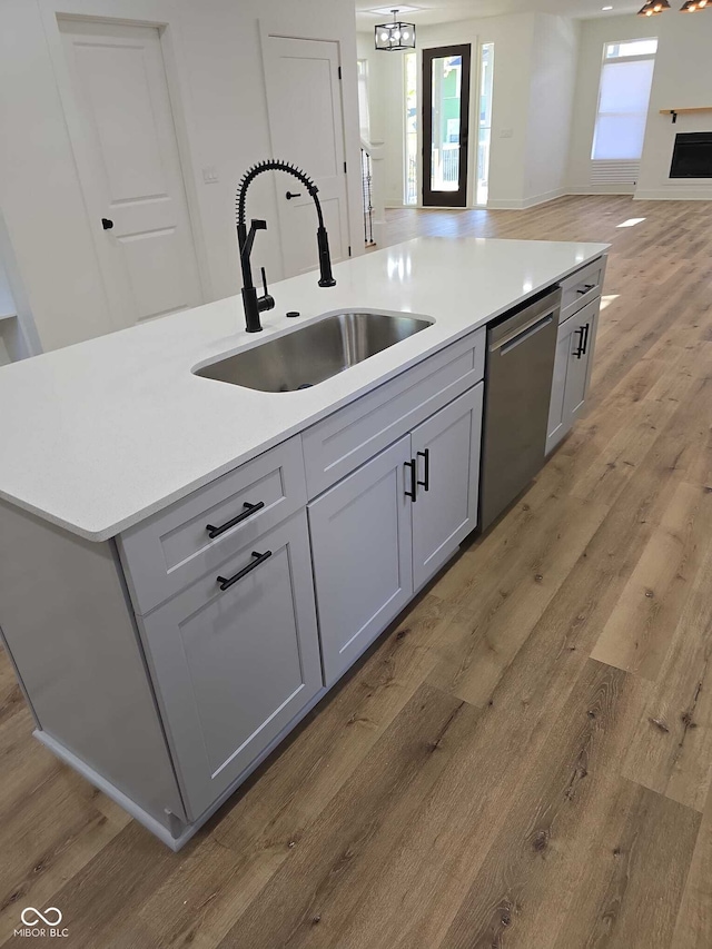 kitchen featuring gray cabinetry, dishwasher, a center island with sink, sink, and light hardwood / wood-style flooring