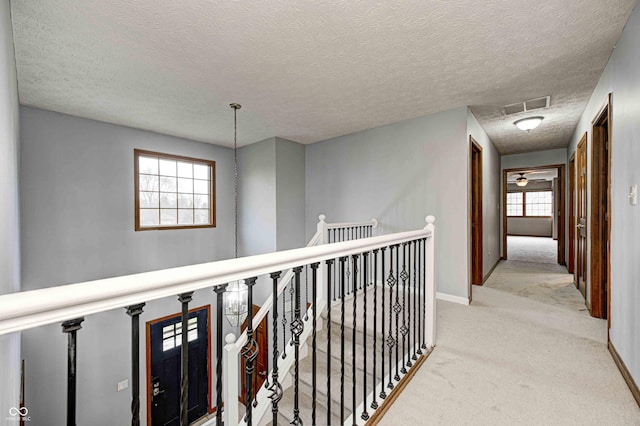 corridor featuring visible vents, light carpet, a textured ceiling, an upstairs landing, and baseboards