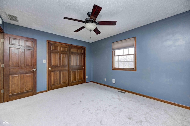 unfurnished bedroom with a textured ceiling, carpet floors, a closet, and ceiling fan