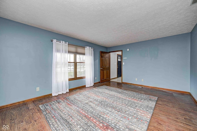 empty room with dark wood-style flooring, visible vents, a textured ceiling, and baseboards