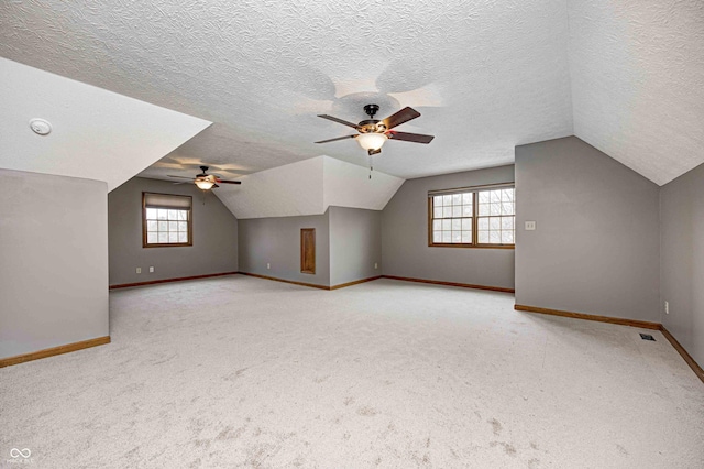 additional living space with light carpet, vaulted ceiling, a textured ceiling, and baseboards