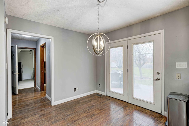 unfurnished dining area with a textured ceiling, dark wood-type flooring, and a notable chandelier