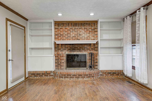 unfurnished living room with built in shelves, dark wood finished floors, a fireplace, and a textured ceiling