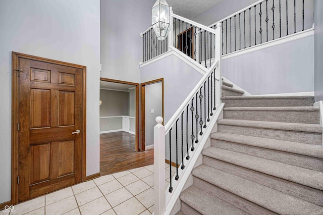 staircase with hardwood / wood-style floors, a towering ceiling, and a notable chandelier