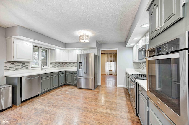 kitchen with tasteful backsplash, stainless steel appliances, light countertops, gray cabinetry, and light wood-type flooring