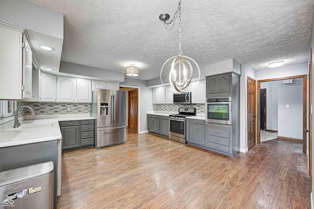 kitchen featuring decorative light fixtures, gray cabinets, wood-type flooring, and appliances with stainless steel finishes