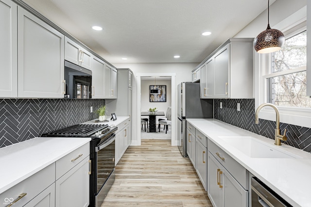 kitchen with decorative backsplash, stainless steel appliances, sink, pendant lighting, and light hardwood / wood-style flooring