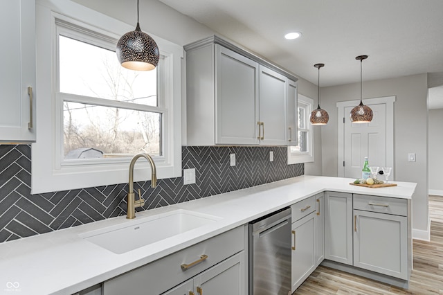 kitchen featuring light wood-type flooring, backsplash, stainless steel dishwasher, sink, and hanging light fixtures