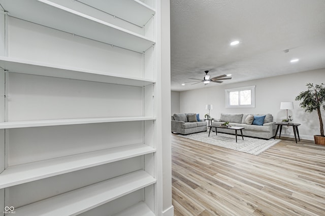 living room featuring ceiling fan, a textured ceiling, and light hardwood / wood-style flooring