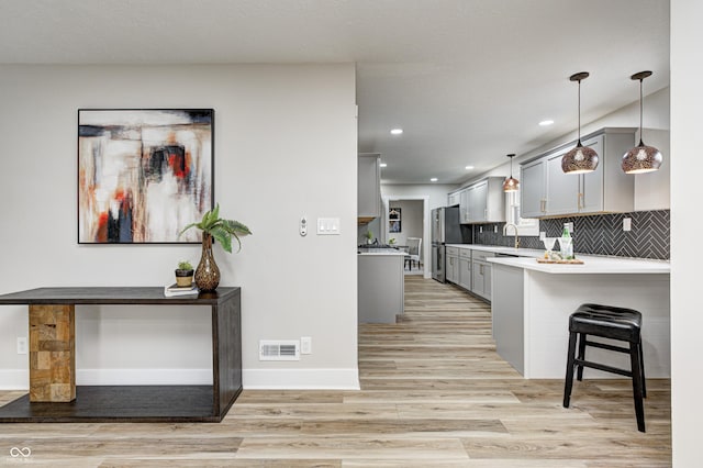 kitchen featuring kitchen peninsula, a kitchen bar, gray cabinetry, light hardwood / wood-style floors, and stainless steel refrigerator