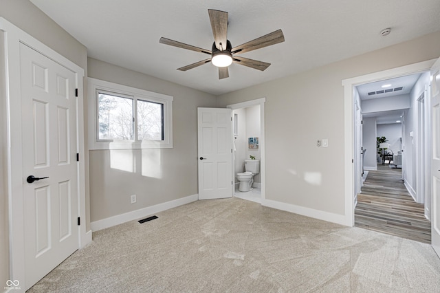 unfurnished bedroom with ceiling fan, light colored carpet, and ensuite bath